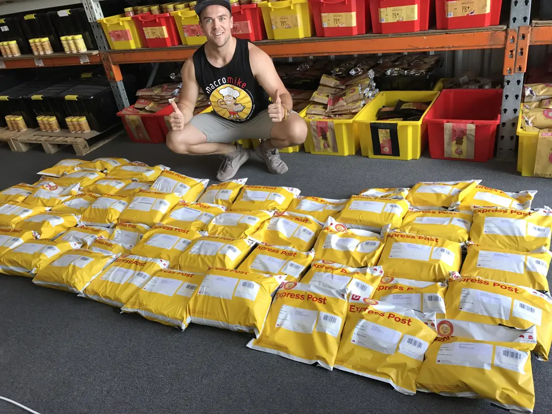 Mike crouching behind rows of yellow Macro Mike satchels ready to ship